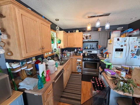 Cluttered kitchen with wooden cabinets, black appliances, white refrigerator, and various items on countertops and shelves