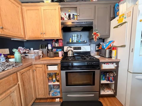 Kitchen interior with wooden cabinets, black stove, white refrigerator, and countertops cluttered with items and cookware