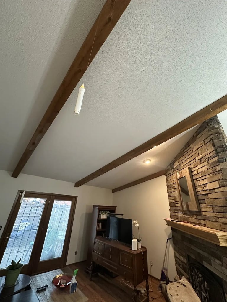 Interior living room with exposed wooden beam ceiling, fireplace with stone surround, wooden furniture, and glass doors