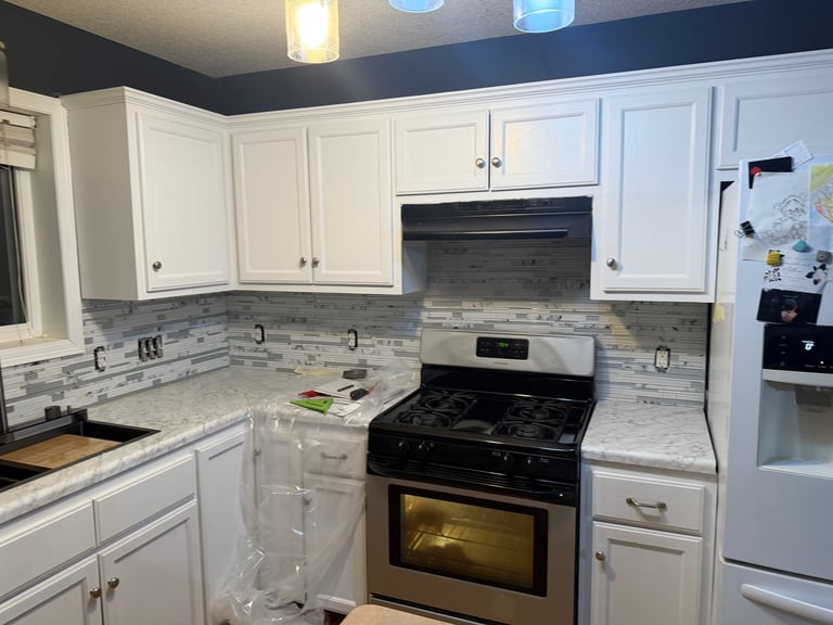 Modern kitchen with white cabinets, gray and white tile backsplash, black gas stove, and stainless steel refrigerator
