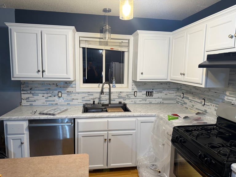 Modern kitchen with white cabinetry, stainless steel appliances, blue backsplash tile, and granite countertops