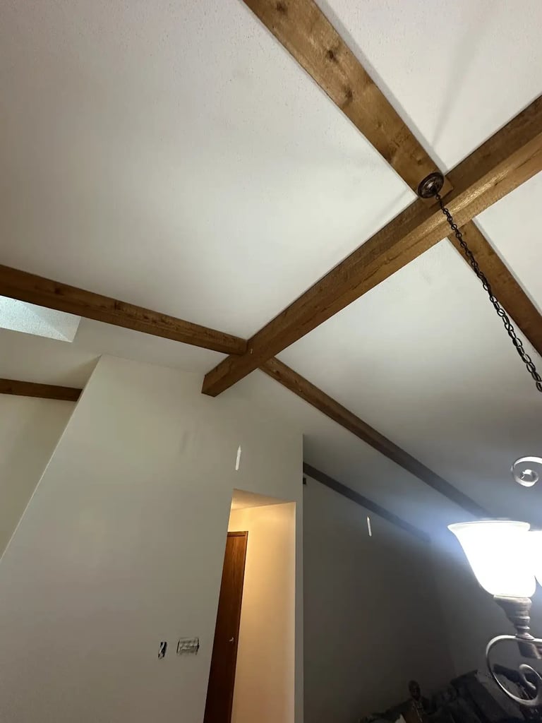 Interior ceiling with exposed wooden beams crossing overhead against white drywall and recessed lighting
