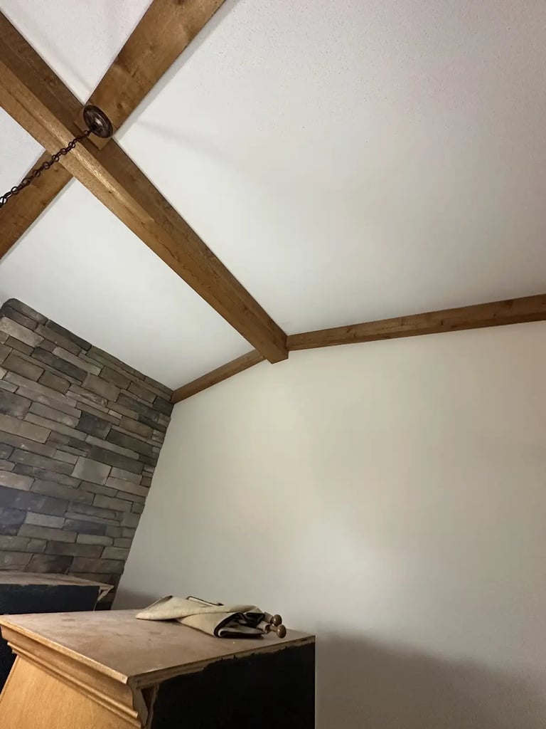 Interior room corner with exposed wooden beams on white ceiling, gray brick accent wall, and wooden desk with items