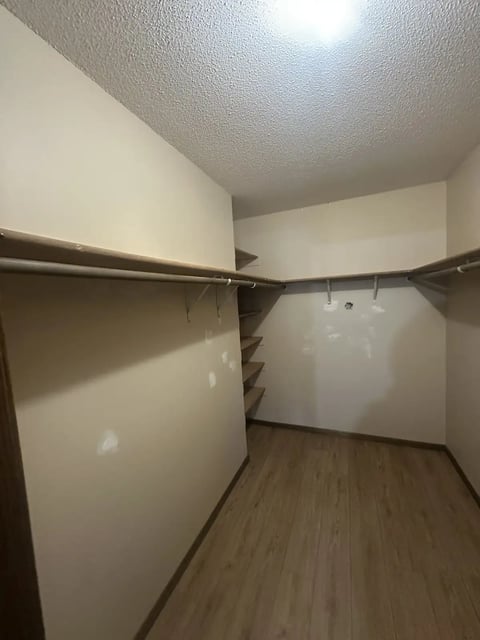 Empty walk-in closet with white walls, textured ceiling, wooden laminate flooring, metal clothing rods, and shelving units on both sides
