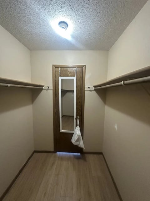 Empty walk-in closet with wood-framed mirror door, metal hanging rods on both sides, white walls, textured ceiling, and LED light fixture